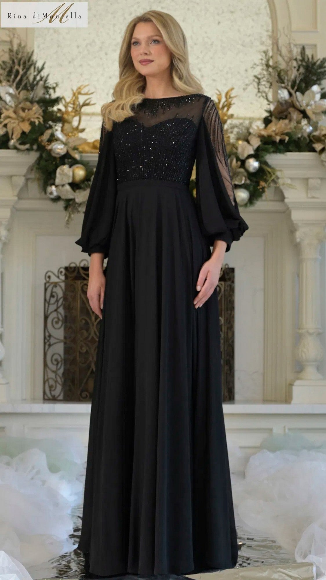 A woman wearing the black Long Formal Dress Rina Di Montella RD3374, featuring a chiffon A-line skirt and beaded bodice, stands indoors in front of a decorated mantle.